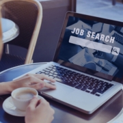 Woman using a laptop with “Job Search” on the screen while holding a coffee cup, symbolizing a mid-year career relaunch through a recruitment agency